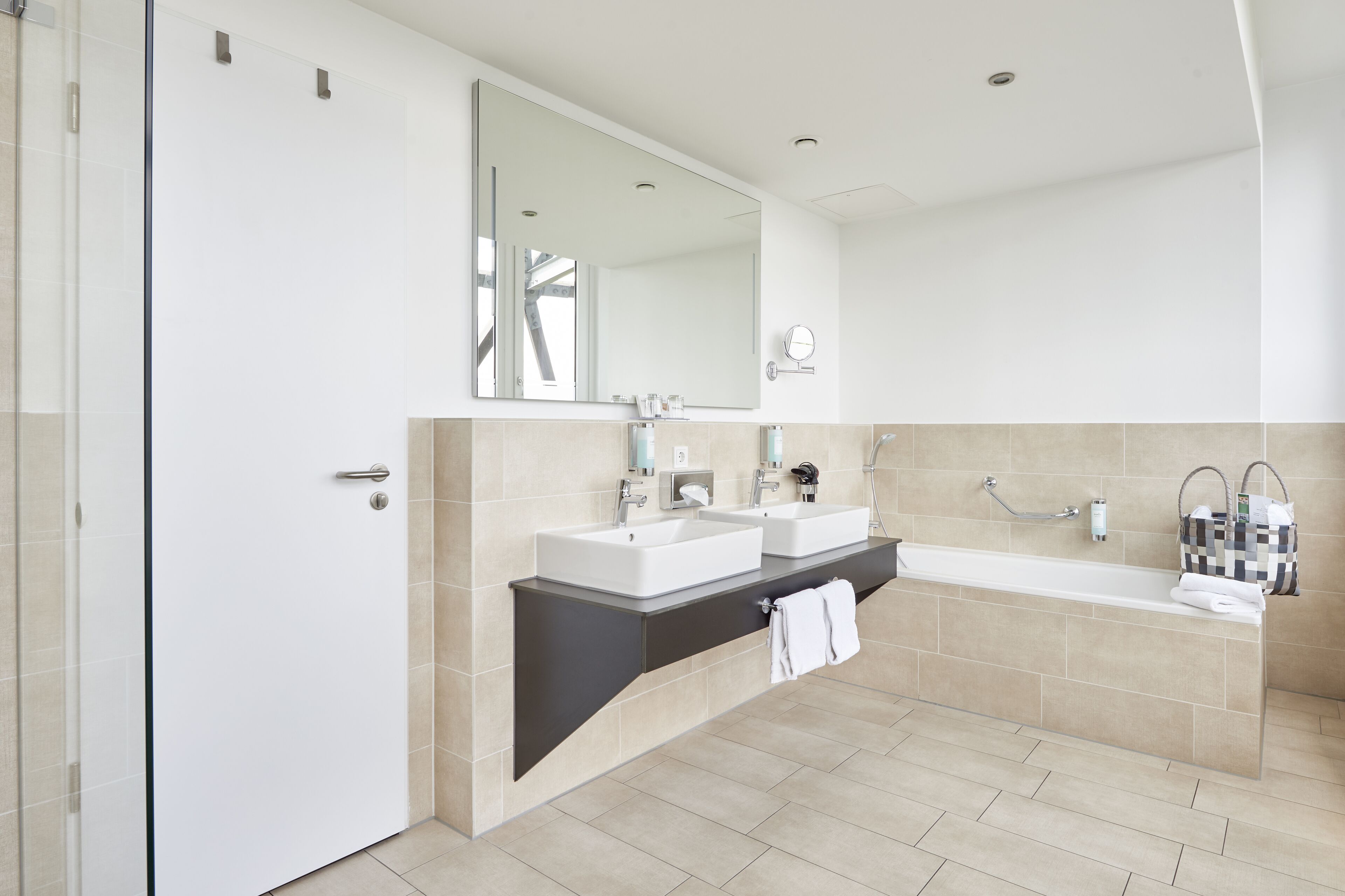 A modern bathroom with two sinks, a large mirror, and a bathtub.
