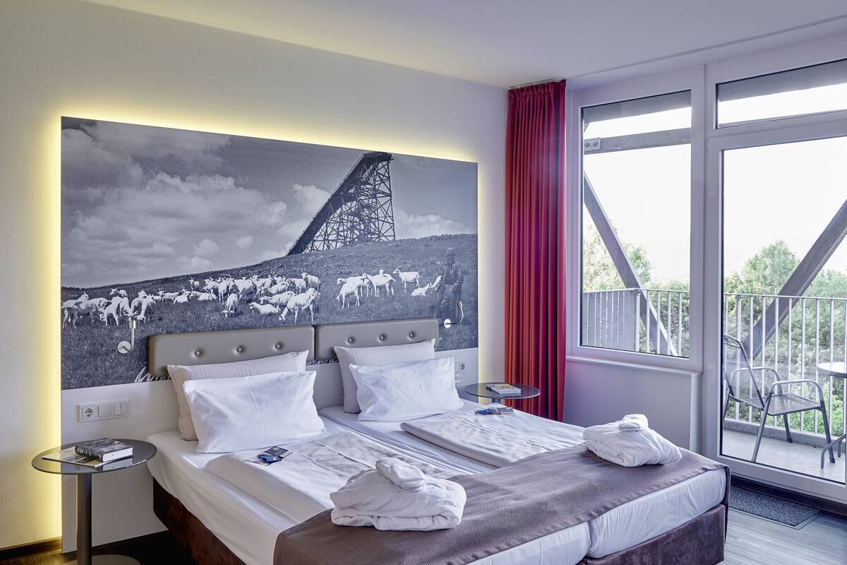 A hotel room with a large bed, two bedside tables, a red curtain, and a balcony with chairs.