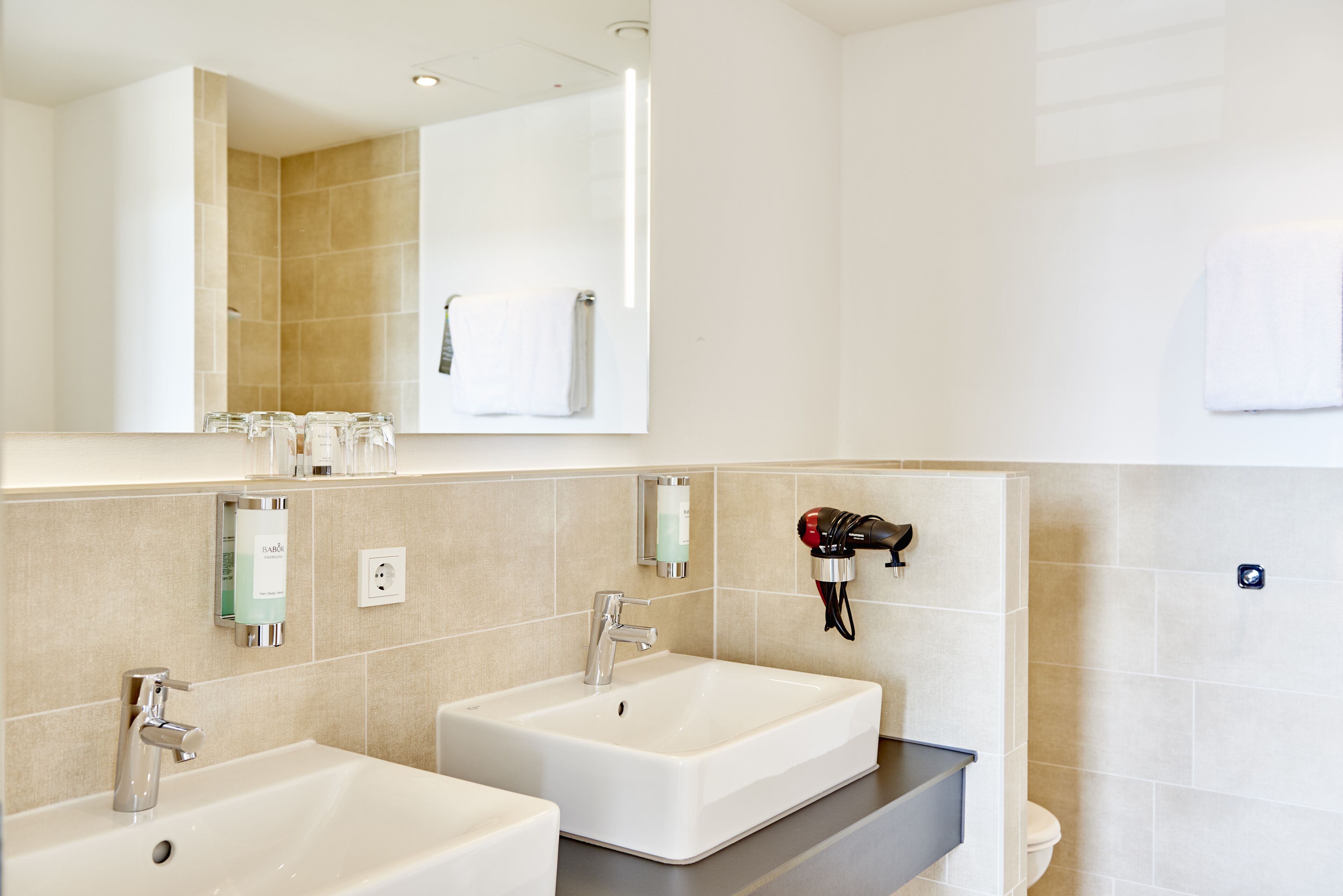Un baño moderno con dos lavamanos, un espejo grande y un perchero para toallas.