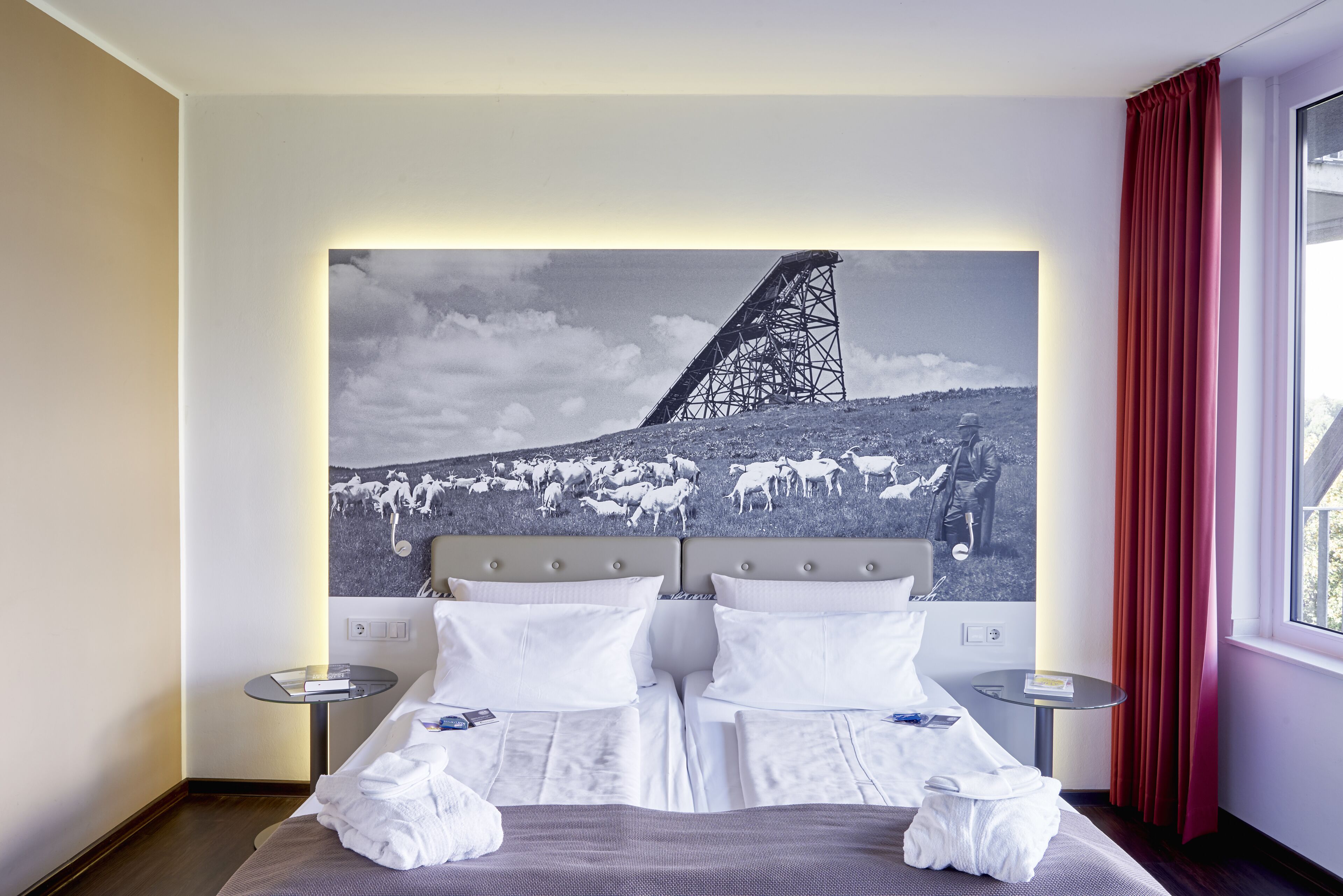 A hotel room with a large bed, two bedside tables, and a wall-mounted artwork depicting a bridge and sheep.