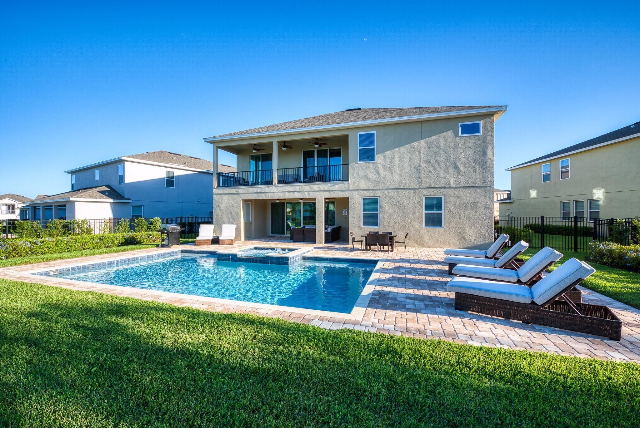 A two-story house with a swimming pool, outdoor seating, and a well-maintained lawn.
