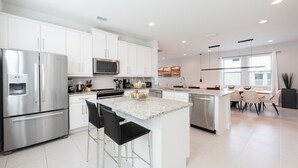 A modern kitchen with white cabinets, stainless steel appliances, a granite countertop island, and a dining area with white chairs.