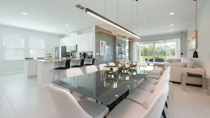 A modern kitchen with white cabinets, a central island, and a dining area with a glass table and white chairs.
