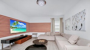 A modern living room with a large flat-screen TV, a sectional sofa, two round coffee tables, and a striped wall. - Striking Home near Disney: Games, Outdoor Kitchen & Waterpark - 7742FF (Kissimmee)