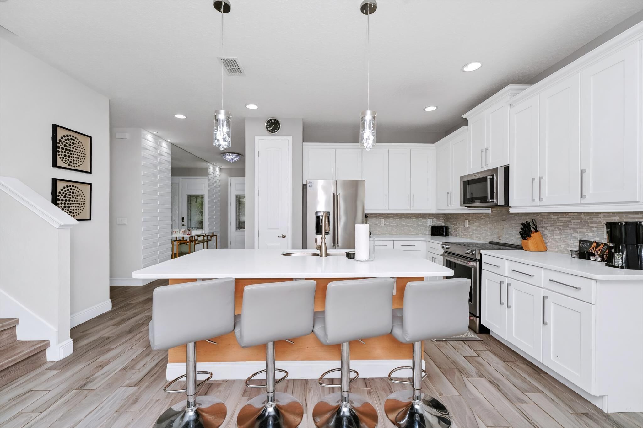 A modern kitchen with white cabinets, a central island with bar stools, stainless steel appliances, and pendant lighting.