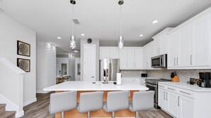 A modern kitchen with white cabinets, a central island with bar stools, stainless steel appliances, and pendant lighting. - Striking Home near Disney: Games, Outdoor Kitchen & Waterpark - 7742FF (Kissimmee)