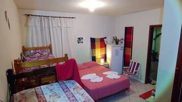 Un dormitorio con cama, una silla, una mesita y una ventana con cortinas.