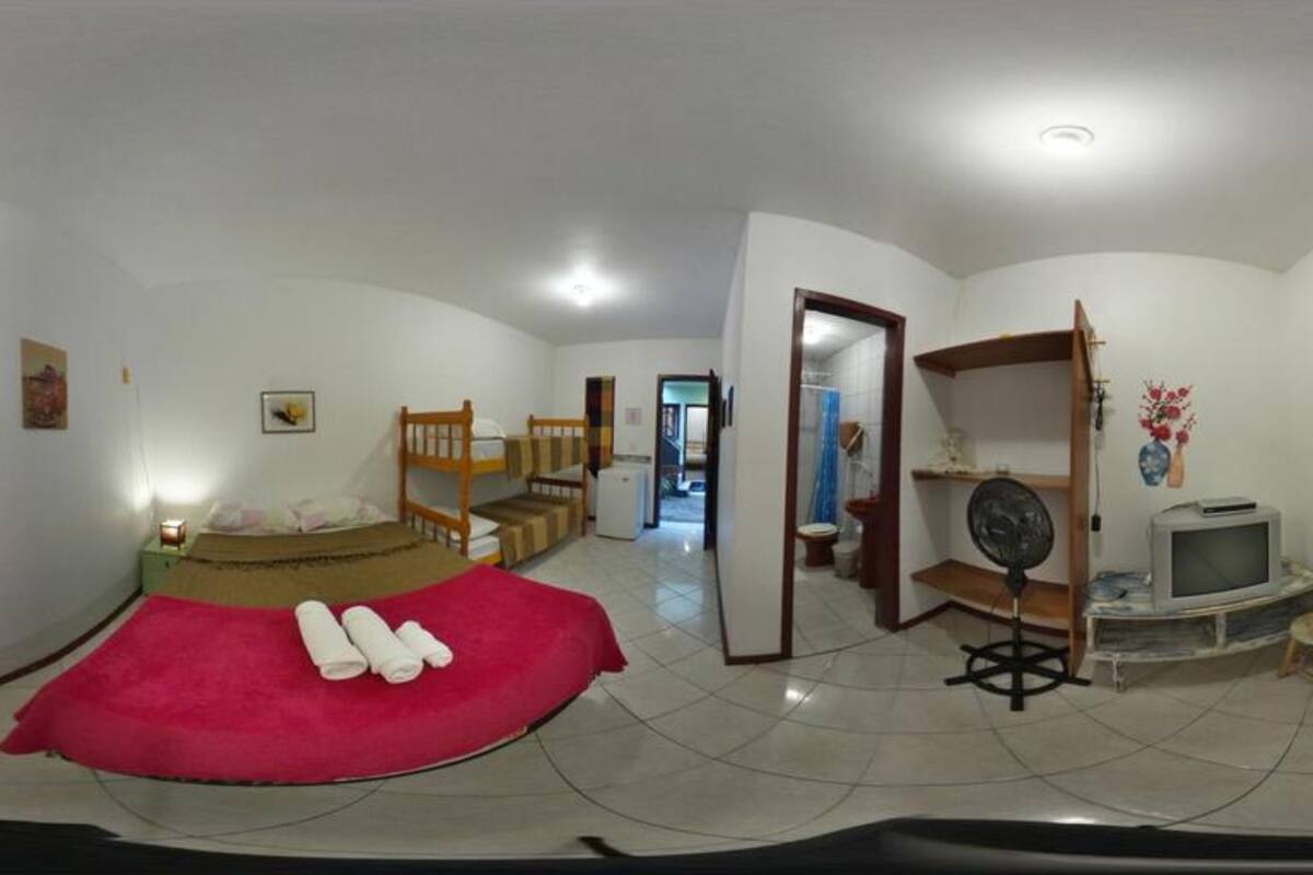 Quarto com uma cama, televisão, ventilador e porta que dá para outro espaço.