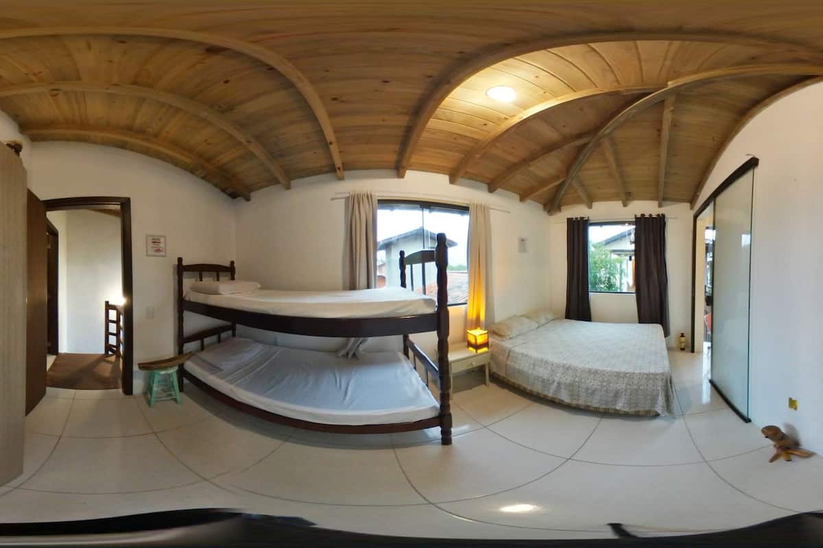 Quarto com beliche, teto de madeira, janela com cortinas e guarda-roupa.