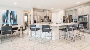 Una cocina moderna con una isla central, taburetes de bar y un comedor con mesa y sillas.