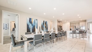 A spacious dining area with a long table and modern chairs, a kitchen with white cabinets, and a clean, minimalist design.