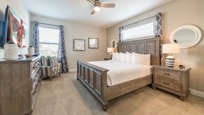 Une chambre à coucher avec un lit en bois, une table de chevet avec une lampe, une commode, un ventilateur de plafond et une fenêtre avec des rideaux.