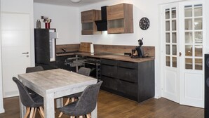 Eine kompakte Küche mit Essbereich, ausgestattet mit einem Holztisch und Stühlen, einem eingebauten Ofen und einer schwarzen Dunstabzugshaube.