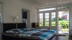 Ein Schlafzimmer mit einem großen Bett, einem Nachttisch mit Lampe und Blick ins Grüne.