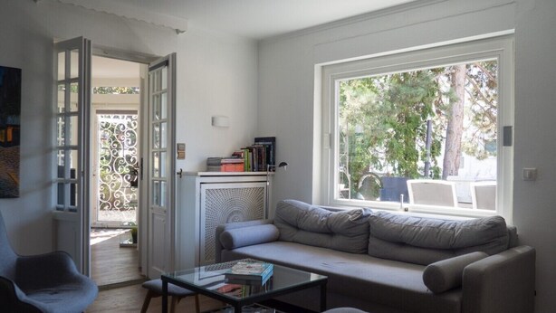 Ein Wohnzimmer mit grauem Sofa, einem Glastisch und einer weißen Kommode mit Büchern.