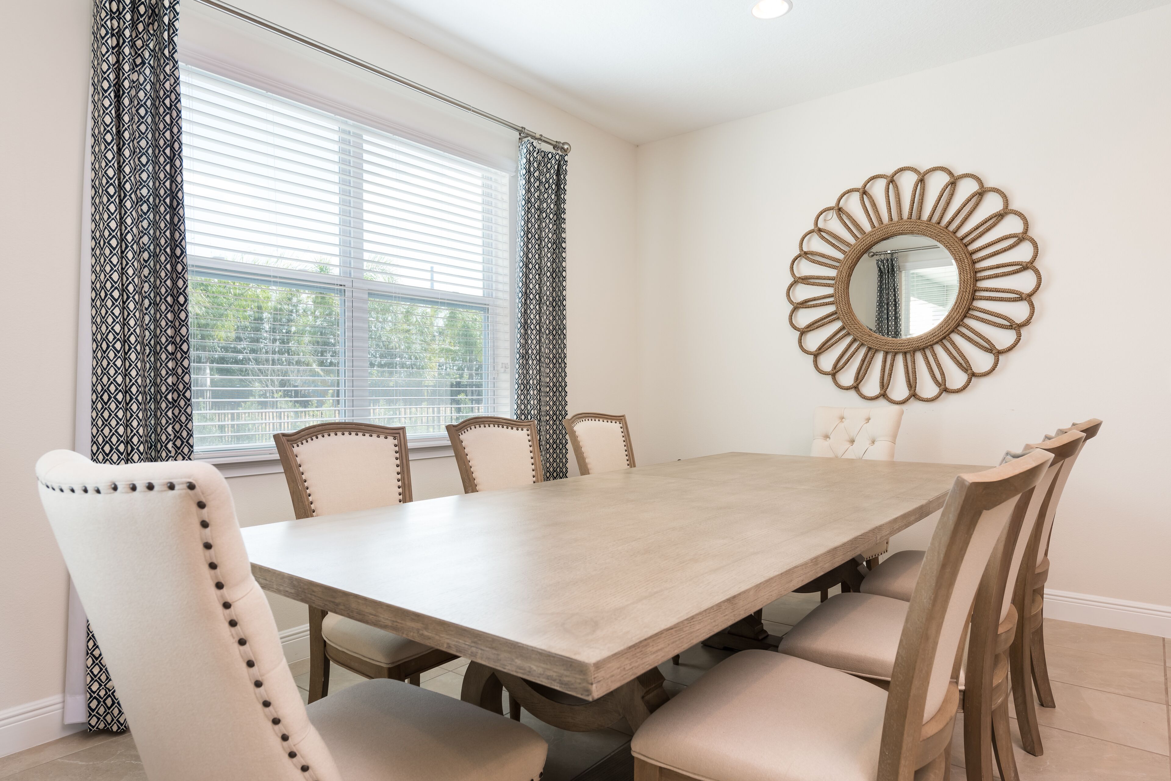 Une salle à manger avec une table rectangulaire, six chaises et un miroir décoratif au mur.