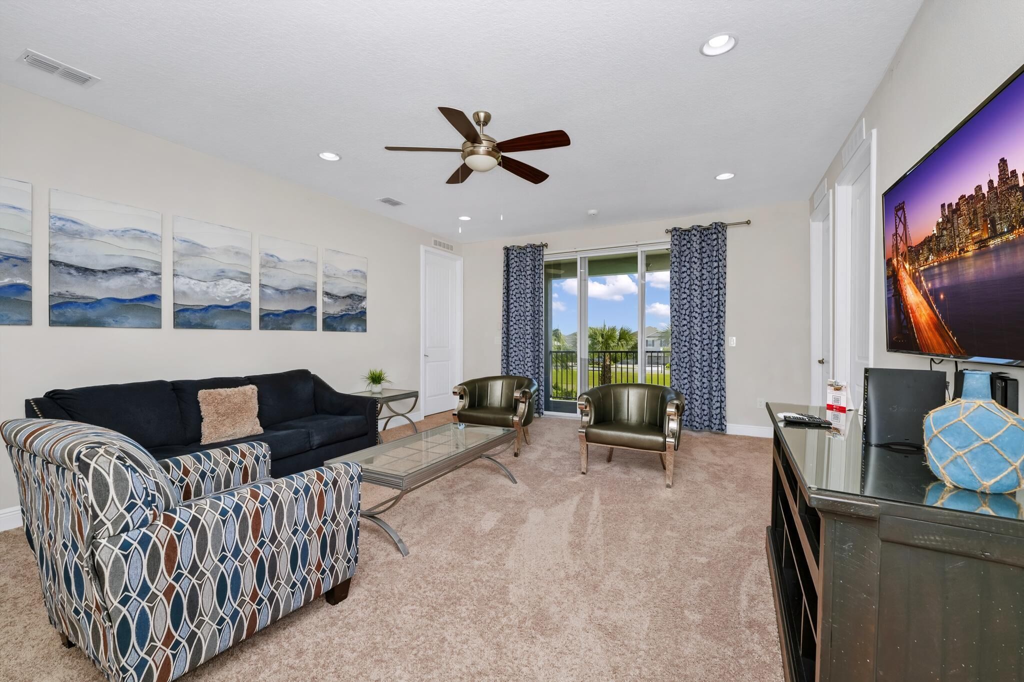 A living room with a sofa, two armchairs, a coffee table, a TV, and a ceiling fan.