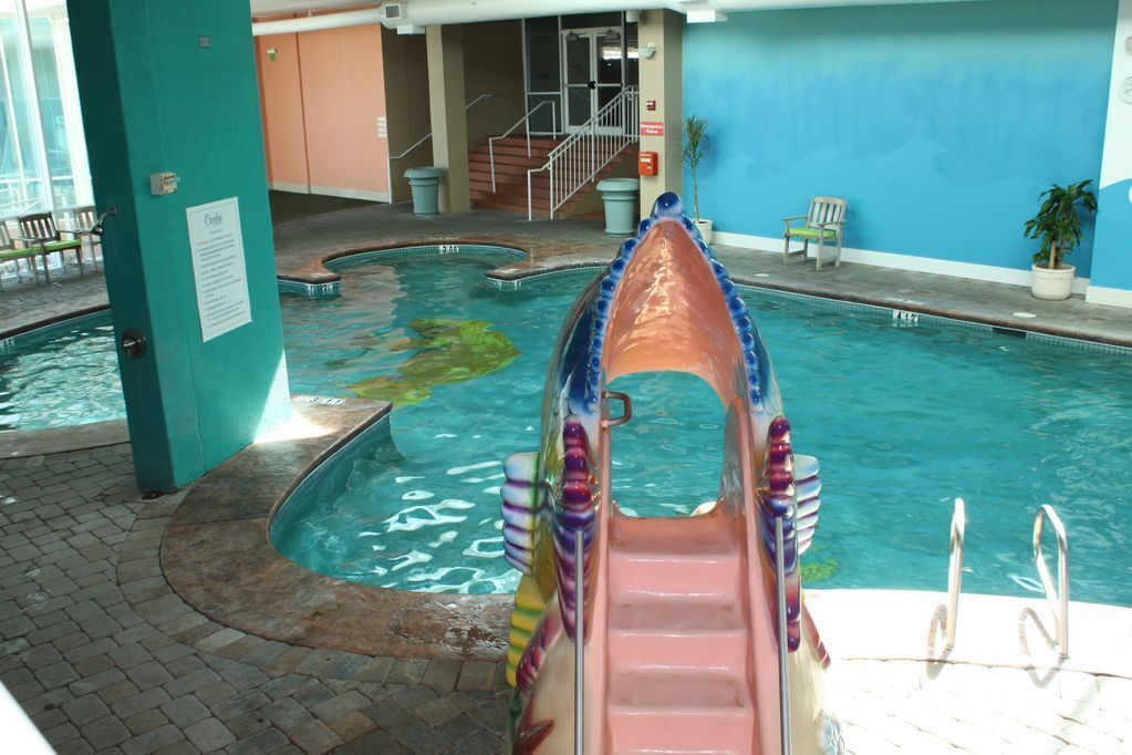 Une piscine intérieure avec un toboggan, un escalier et un espace détente comprenant des chaises et une plante en pot.