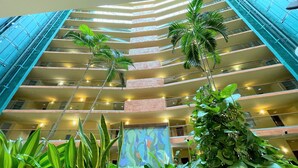 A multi-story hotel interior with a central atrium, featuring a modern design with glass railings and a variety of indoor plants.