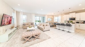 A spacious living area with a large TV, sofas, a coffee table, and a kitchen with bar stools. - Luxury Home near Disney: Themed Rooms, Air Hockey & Waterpark - 7699GR (Reunion)
