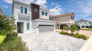 A modern two-story house with a garage, a well-maintained lawn, and a clear sky. - Luxury Home near Disney: Themed Rooms, Air Hockey & Waterpark - 7699GR (Reunion)