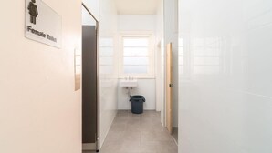 Un couloir étroit avec un panneau indiquant les toilettes pour femmes, un lavabo et une poubelle.