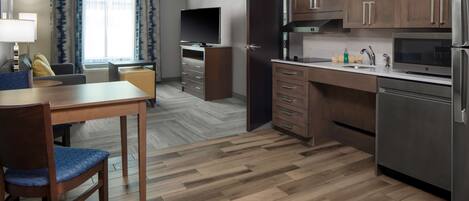 Una habitación de hotel moderna con zona de comedor, kitchenette y un gran ventanal con cortinas.