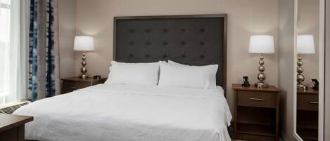 A hotel room with a large bed, two bedside tables with lamps, a mirror, and a window with curtains.
