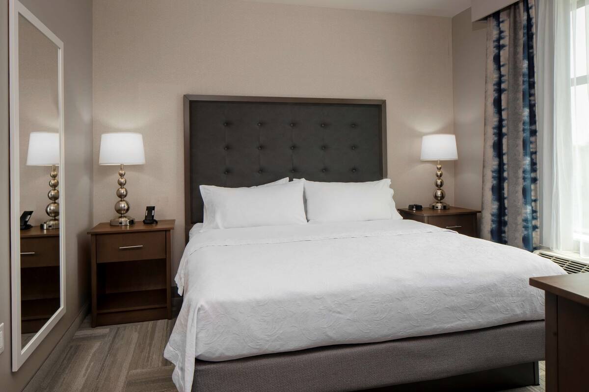 A neatly made bed with a tufted headboard, two bedside tables with lamps, and a large mirror on one wall.