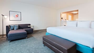 A hotel room with a bed, a sofa, a bench, a desk, and a framed picture on the wall.