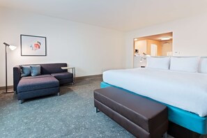 A hotel room with a bed, a sofa, a bench, a desk, and a framed picture on the wall. - Hilton Garden Inn Homestead (Homestead)
