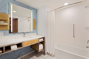A modern bathroom with a large mirror, white sink, and shower area. - Hilton Garden Inn Homestead (Homestead)