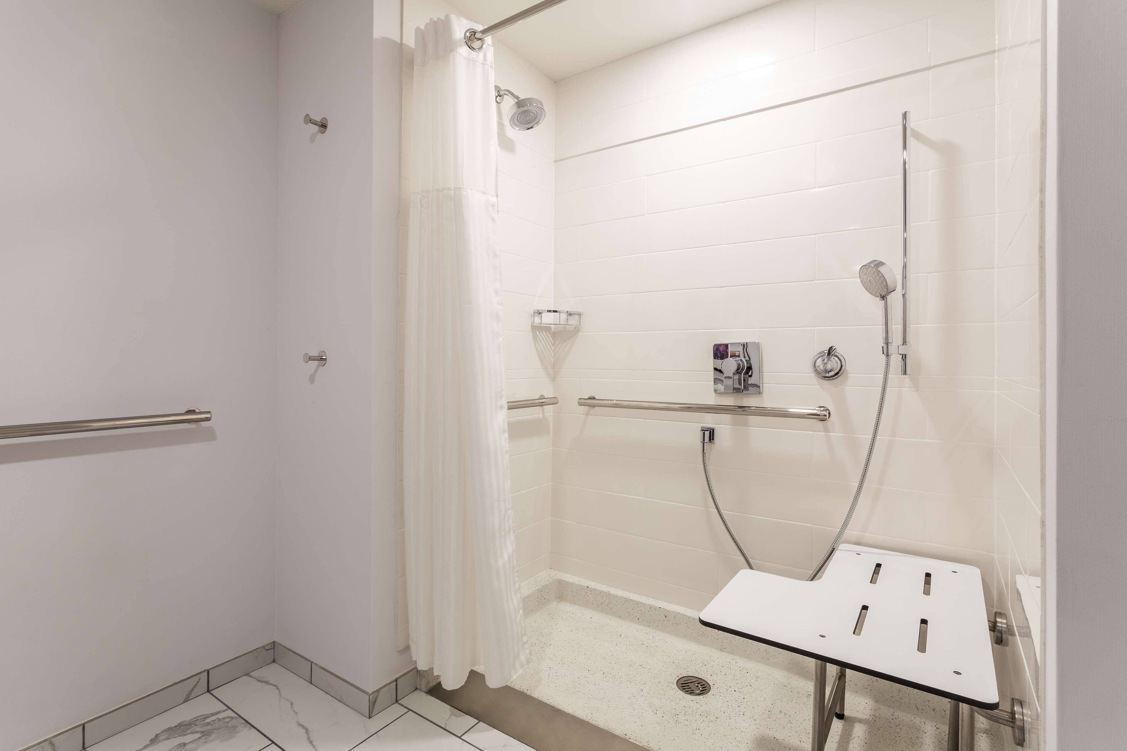 A wheelchair-accessible shower with a grab bar, a handheld showerhead, and a handheld showerhead with a hose.