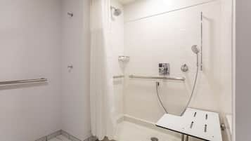 Ducha accesible en silla de ruedas con barra de apoyo y cabezal de ducha manual.
