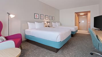 A hotel room with two beds, a desk, a chair, a TV, and artwork on the wall.