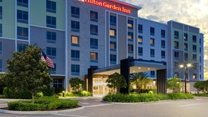 Un hôtel Hilton Garden Inn doté d’une façade moderne, d’un drapeau et d’une entrée bien éclairée.
