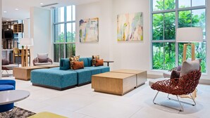 Un salon moderne avec un canapé bleu, une table basse en bois et un fauteuil en osier rouge. De grandes fenêtres offrent une vue sur la verdure environnante.