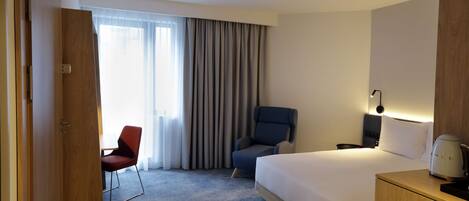 A hotel room with a bed, a desk, a chair, a lamp, and a coffee maker.