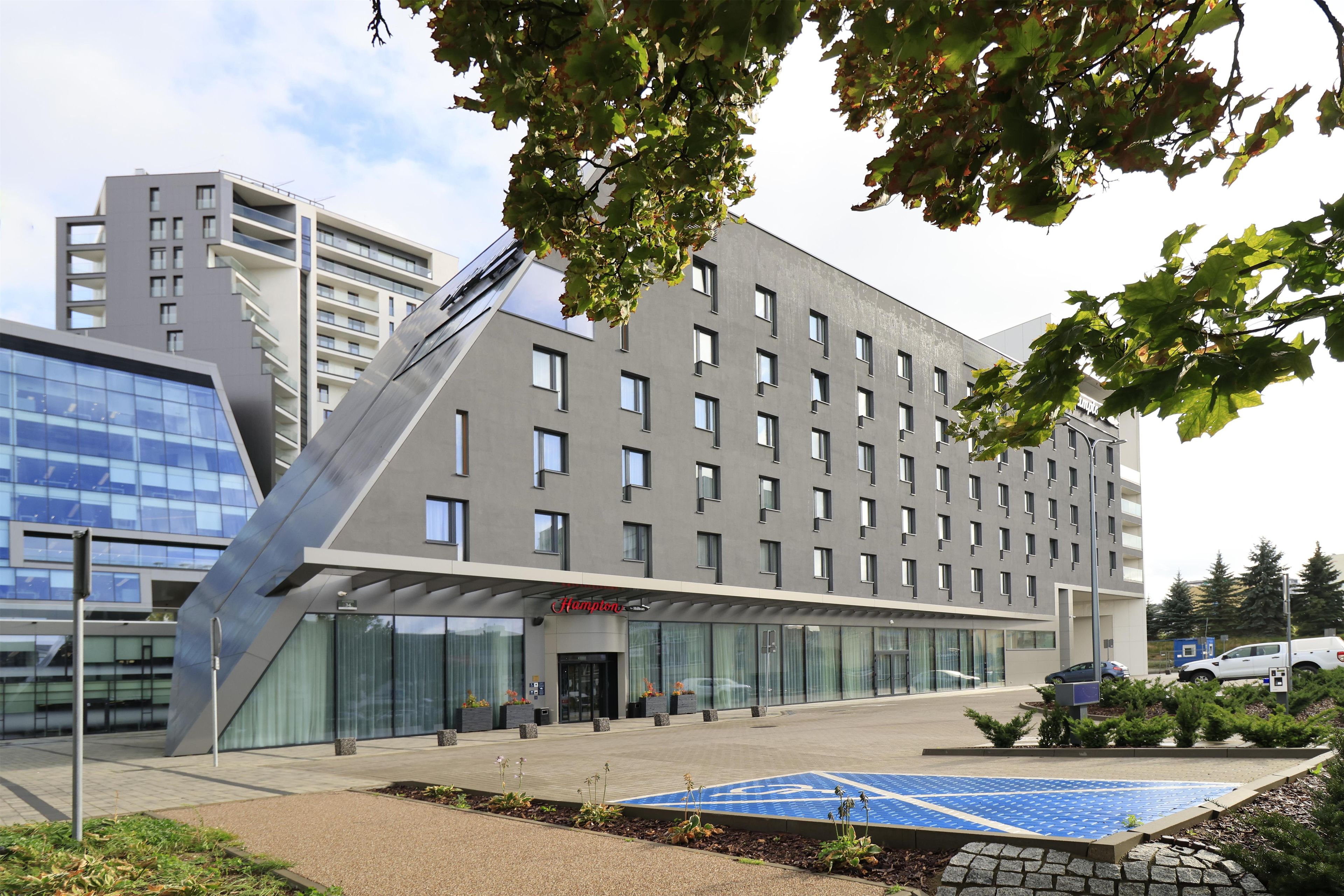 A modern hotel with a flat roof, large windows, and a sign reading 'Hampton.'