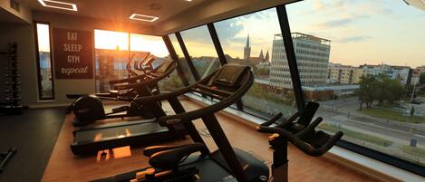 A gym with treadmills, exercise bikes, and a large window with a city view.