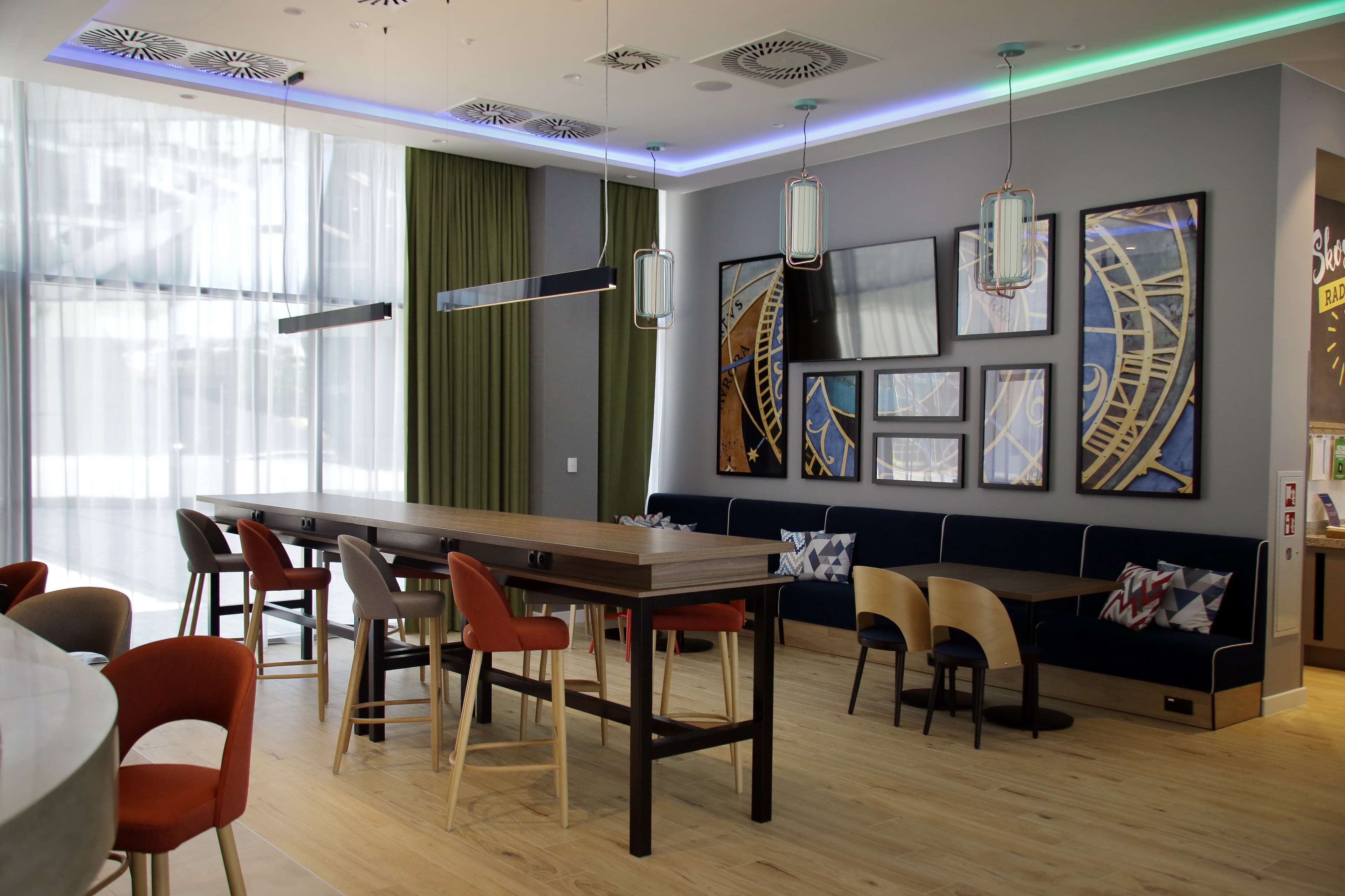 A modern dining area with a long wooden table, red and beige chairs, and a dark blue sofa.