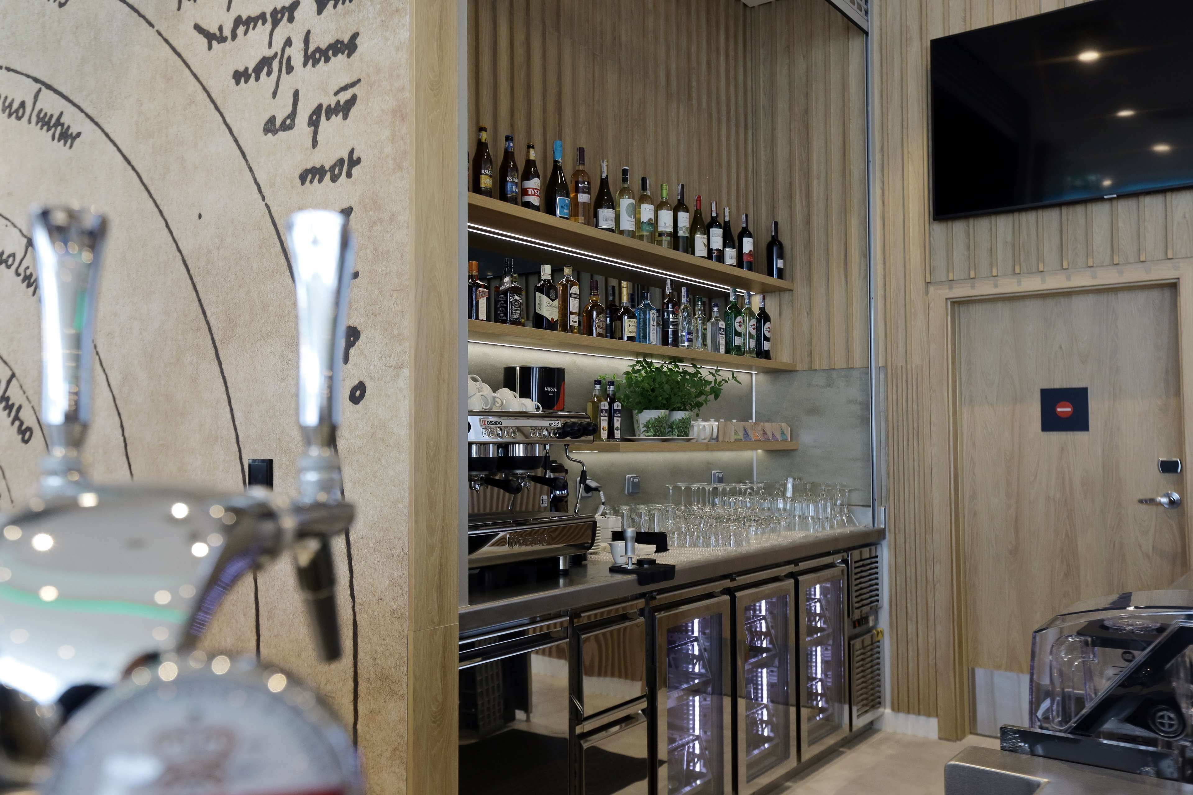 A bar area with a beer tap, shelves of liquor bottles, a coffee machine, and a TV mounted on the wall.
