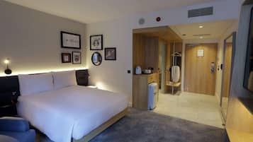 Ett modernt hotellrum med en stor säng, ett skrivbord, en garderob och ett badrum som syns genom en öppen dörr.