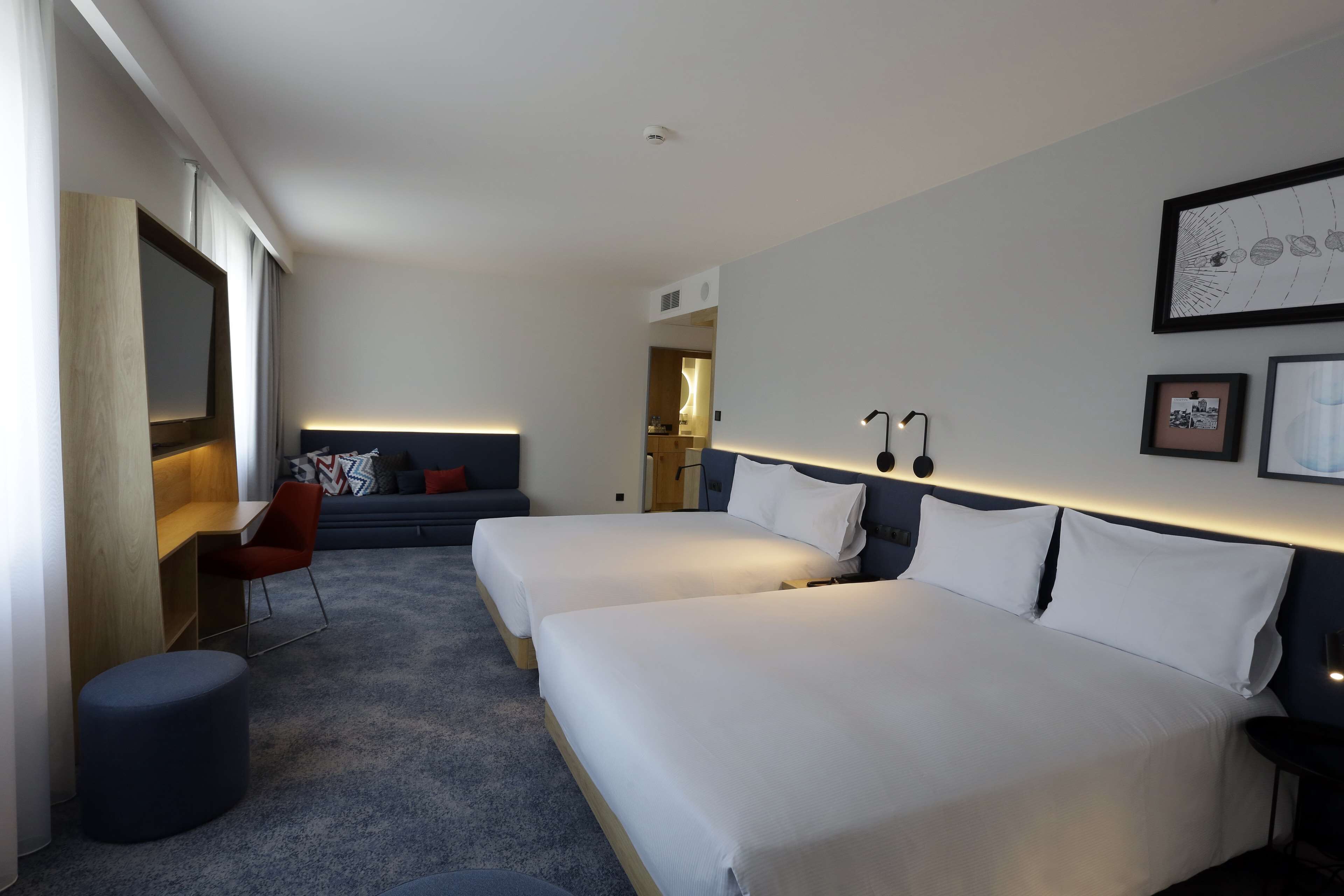 A modern hotel room with two beds, a desk, a chair, and a large window.