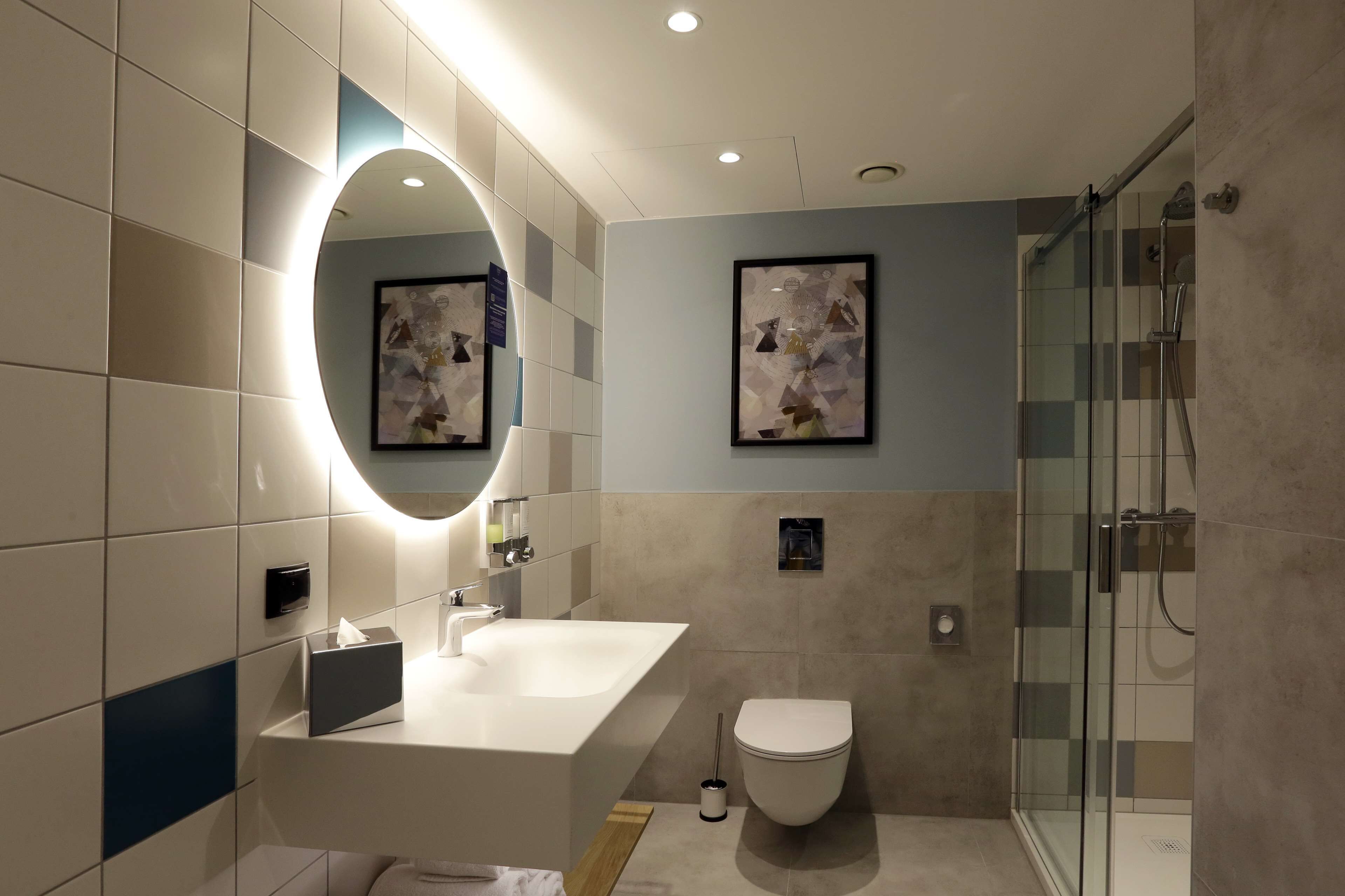 Un baño moderno con un espejo grande, un lavamanos, un inodoro y una cabina de ducha de vidrio.