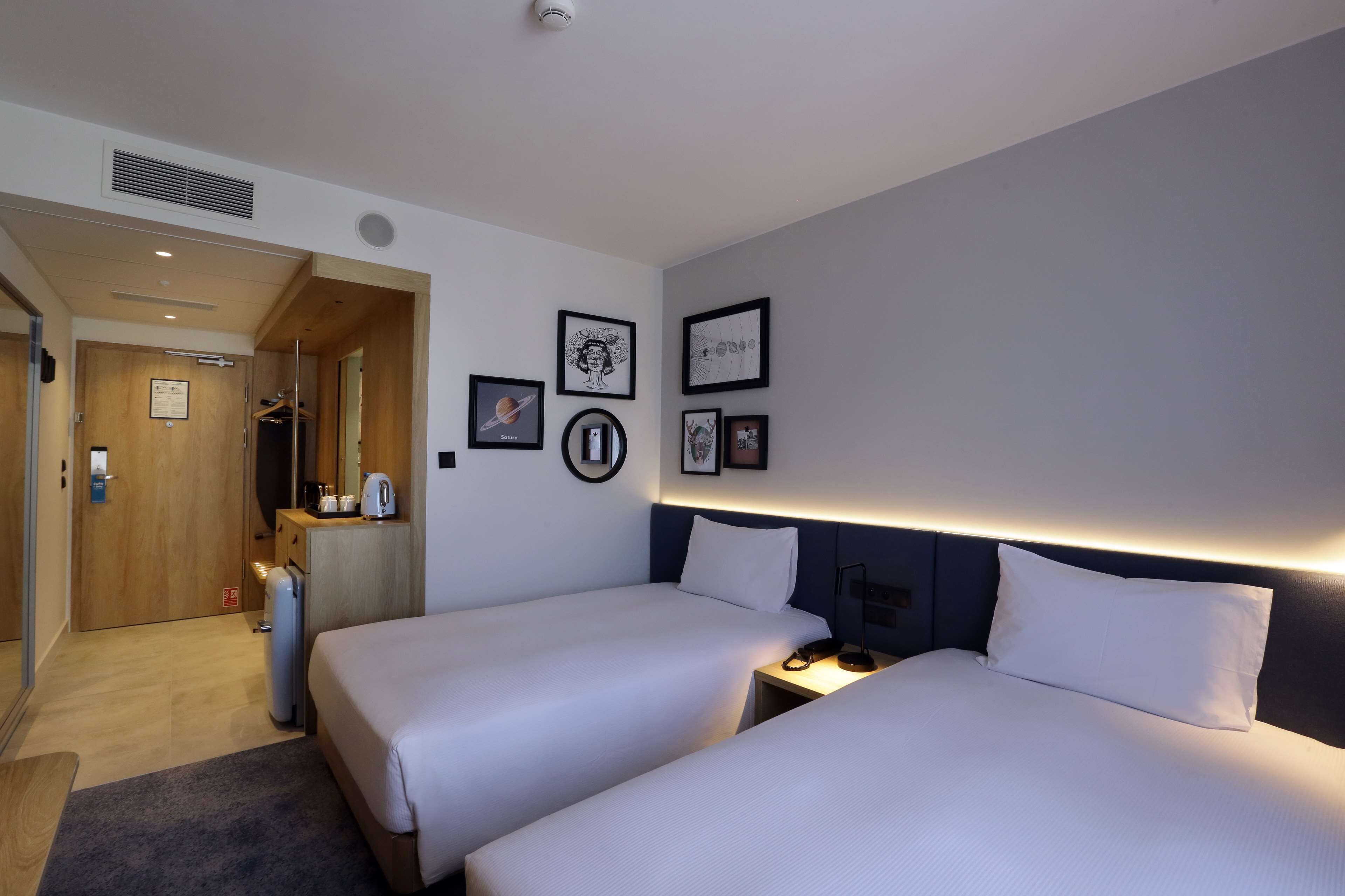 Habitación de hotel con dos camas, un escritorio, una silla, un armario y un baño visible a través de una puerta abierta.