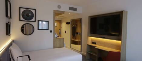 A hotel room with two beds, a TV, a mirror, and a shower area.
