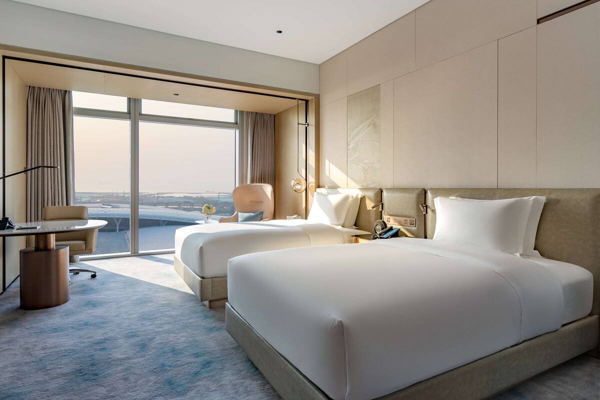 A hotel room with two beds, a desk, and a view of the airport.