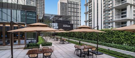 An outdoor patio area with tables and chairs, umbrellas, and a Hilton sign in the background.