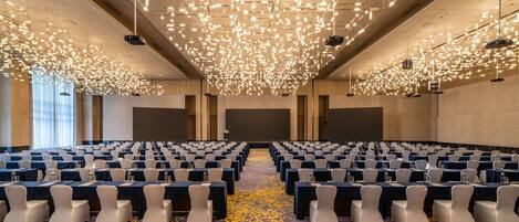 A conference room with rows of tables and chairs, a patterned carpet, and a ceiling with numerous lights.